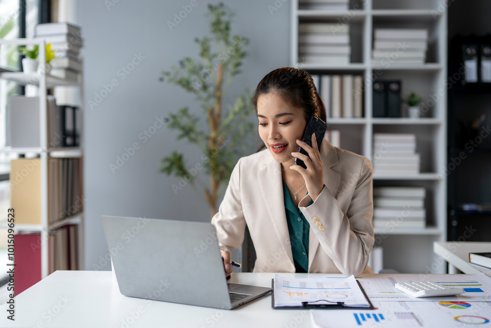 A woman is talking on her cell phone while sitting at a desk with a laptop A woman is talking on her cell phone while sitting at a desk with a laptop