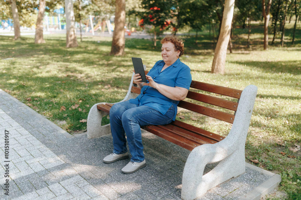 Fototapeta premium Smiling Older Woman Engaging with Her Tablet Surrounded by Nature