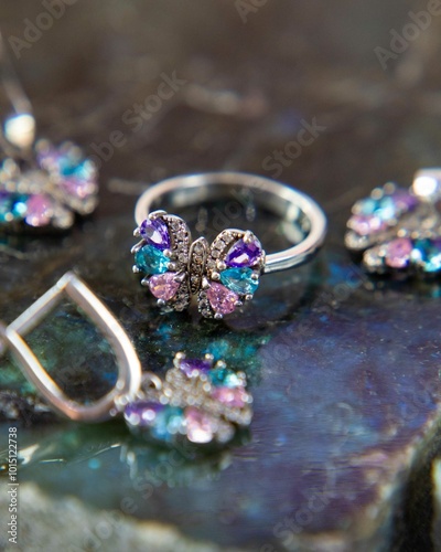 Silver butterfly ring and earrings with colorful gems on stone background