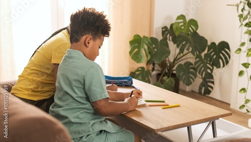 Little boy coloring in book with young sister on table at home