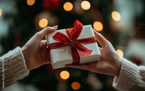 Close-up of hands exchanging a beautifully wrapped gift box with a red ribbon, symbolizing holiday giving, connection, and festive celebration in a cozy, warm setting surrounded by twinkling lights.