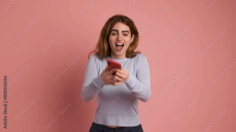 Surprised young redhead lady using mobile phone in pink background Surprised young redhead lady using mobile phone in pink background