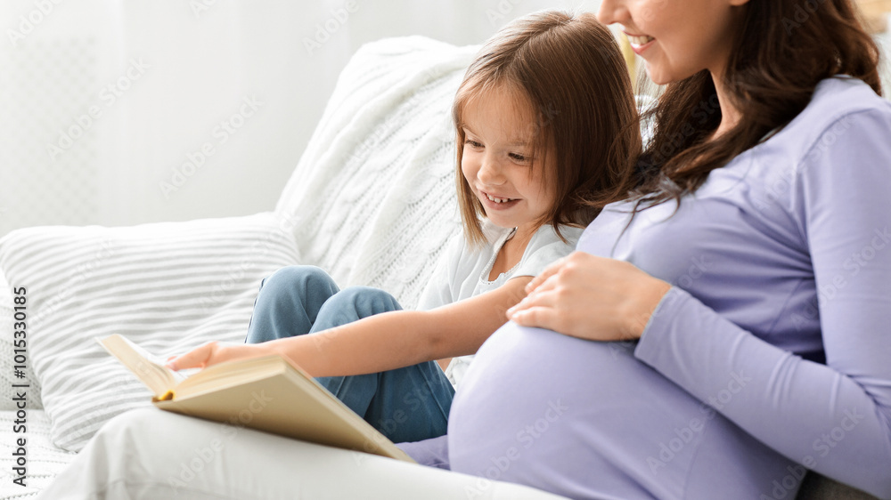 Little daughter and pregnant mom enjoying time together, sitting on sofa at home and reading book, empty space Little daughter and pregnant mom enjoying time together, sitting on sofa at home and reading book, empty space
