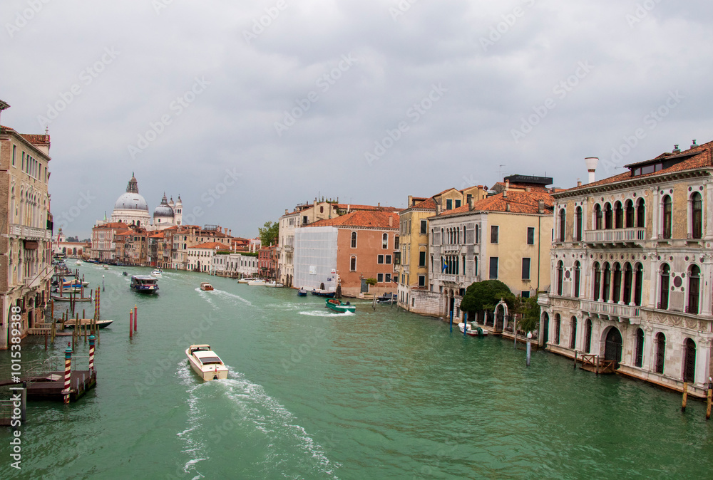 Fototapeta premium Venetian Grand Canal with Historic Buildings and Boats. View of the iconic Grand Canal in Venice, Italy, featuring historic buildings, boats, and the Basilica of Santa Maria della Salute.