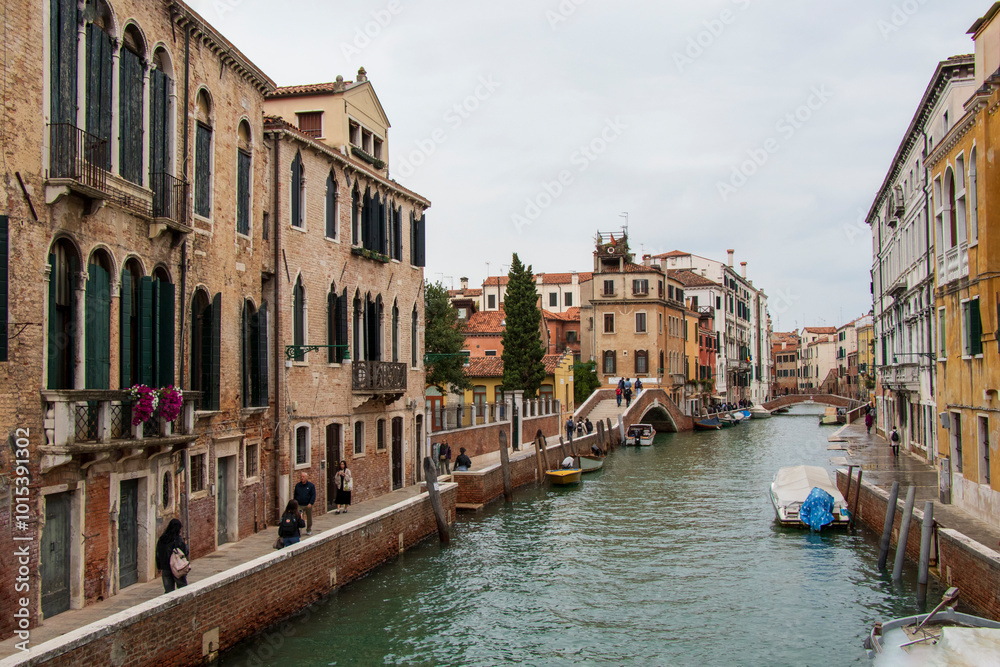 Naklejka premium Venetian Canal Scene with Historic Architecture and Bridge. A vibrant canal in Venice with historic buildings, a pedestrian bridge, and boats, under a colorful sky.