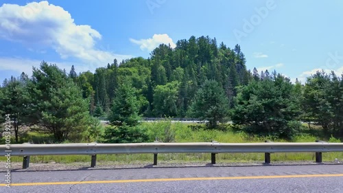 Driving plate front left side driver point of view. Car pov. Driver window side driving view. ON-11, Burk's Falls, Pickerel Lake POV driving on Ontario Highway 11 passing lush green forests.