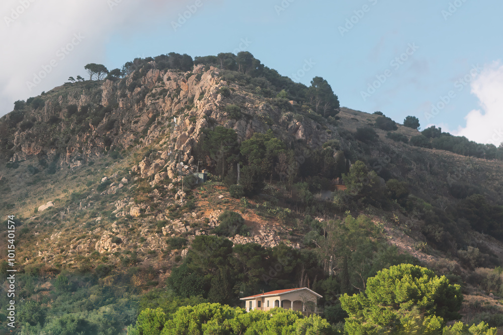 Obraz premium Majestic mountain featuring a house at its peak, set against a backdrop of expansive skies and rugged terrain