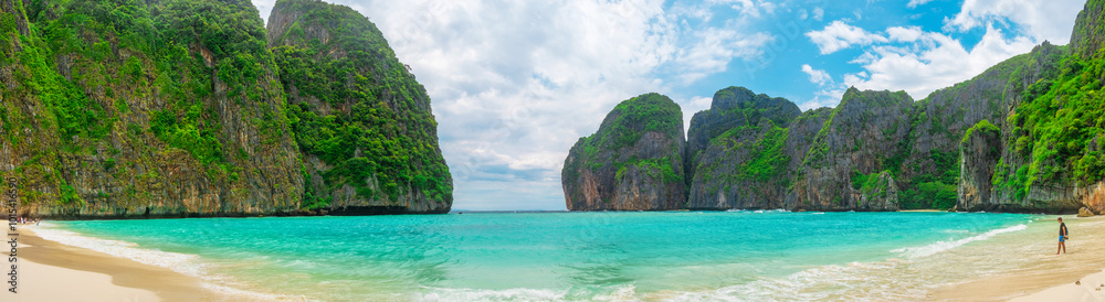 Fototapeta premium Panoramic view of tropical sandy beach Maya Bay with turquoise water ocean on Phi Phi islands, Krabi, Thailand. Male traveler on idyllic beach with mountains and green plants. Travel and tourism