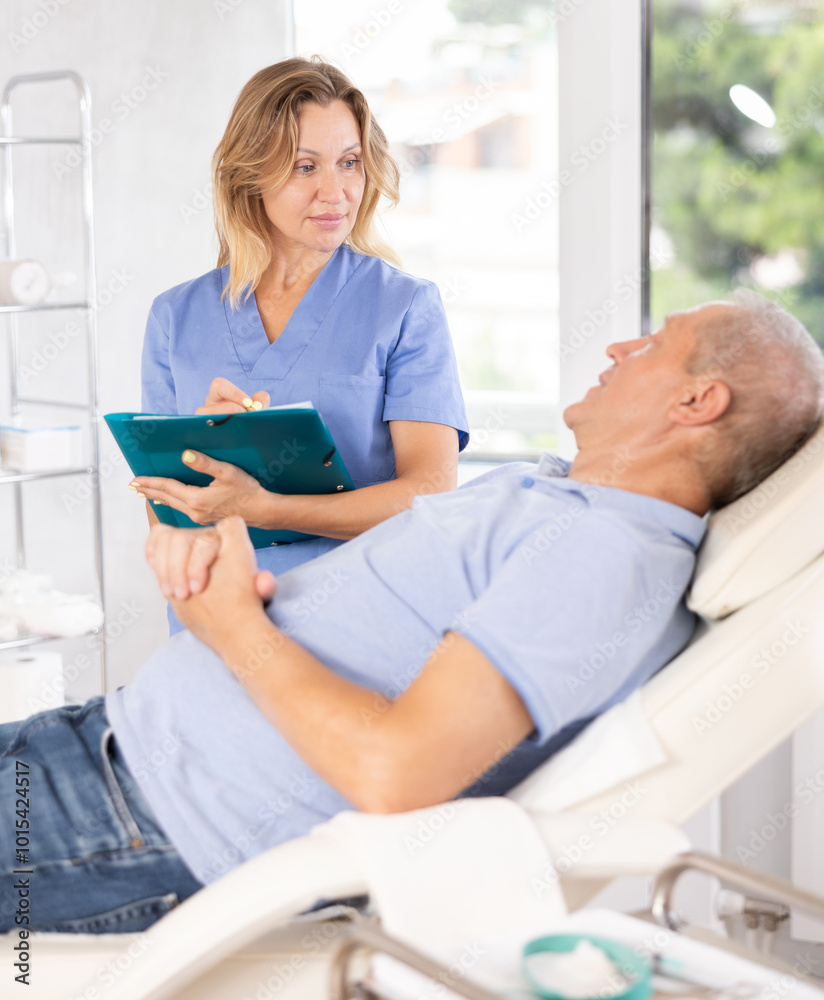 Obraz premium Female doctor conducts survey of elderly male patient after procedure and records data in client medical record