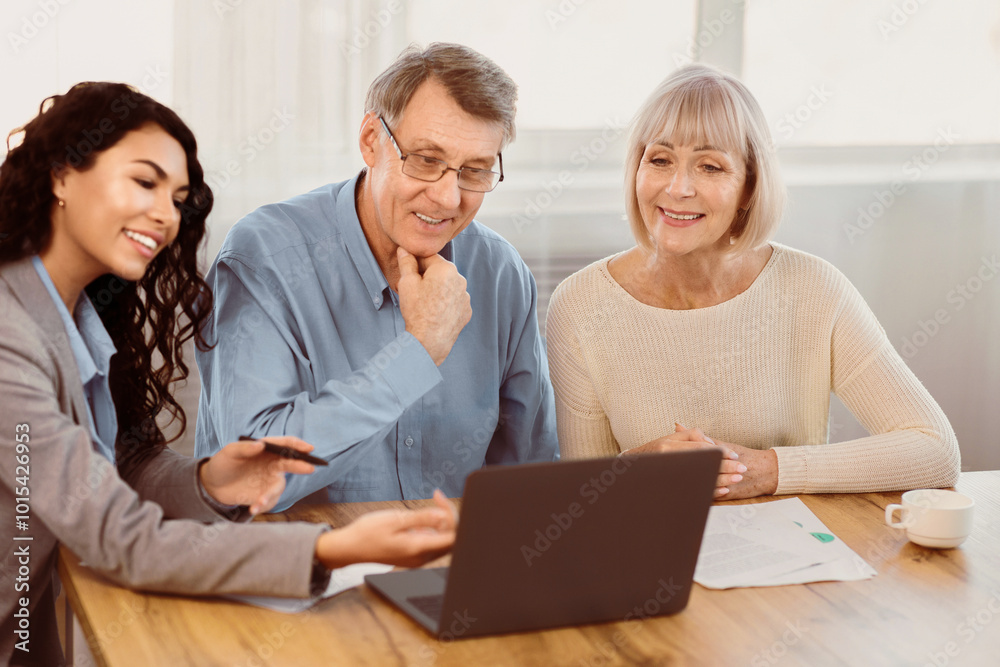 Preparing For A Trip. Mexican travel agent working with elderly clients and offering them tours at office using laptop Preparing For A Trip. Mexican travel agent working with elderly clients and offering them tours at office using laptop