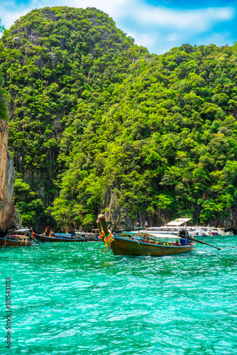 Traditional Thai wooden long-tail boats floating in turquoise water bay with green cliffs on sunny day on Phi Phi islands, Krabi, Thailand. Sailing to Maya Bay beach. Vertical orientation