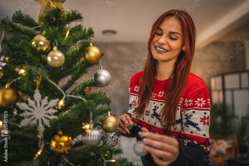 Young woman decorate a Christmas tree with festive ornaments at home