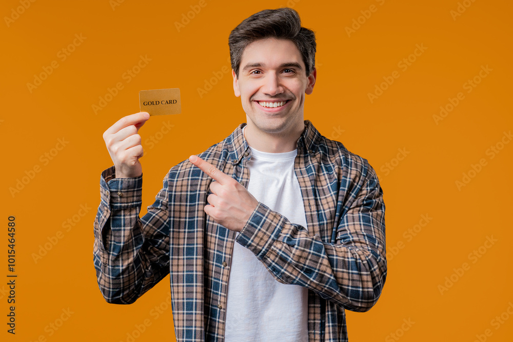 Successful man in orange polo shirt showing unlimited gold credit card on yellow studio background. Student, money concept. Successful man in orange polo shirt showing unlimited gold credit card on yellow studio background. Student, money concept.