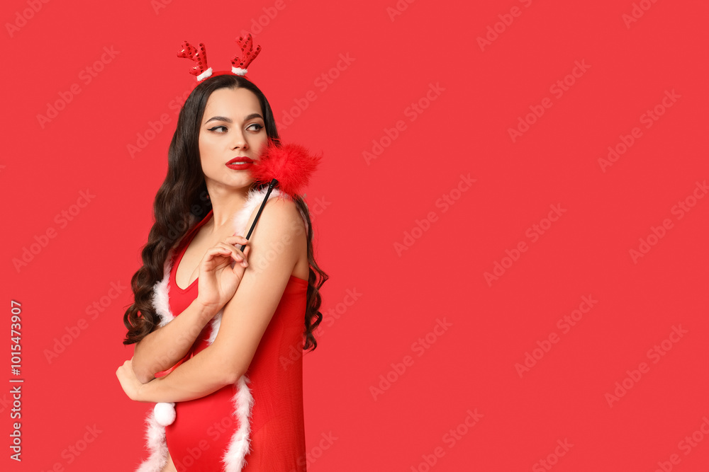 Beautiful young sexy woman with Christmas deer horns and feather stick on red background Beautiful young sexy woman with Christmas deer horns and feather stick on red background