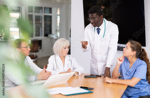 Middle-aged physician engaged in discussion with doctors and nurse sitting around the table photo