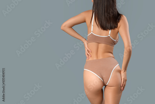 Slim young woman in beige cotton underwear on grey background, back view