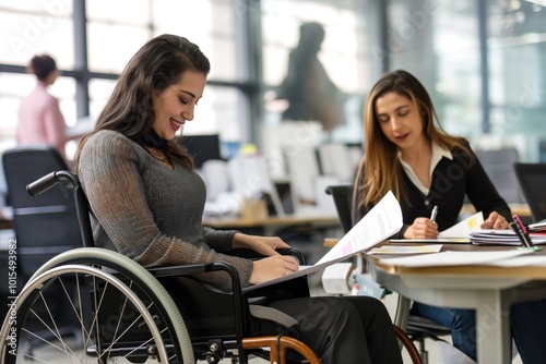 Businesswoman in wheelchair works with female colleague in office. Coworker sits in black chair, surrounded by papers, books. Typical office environment with window, desk in background. Woman in