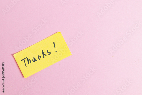 Yellow small note with the word thank you on a pink background in the center