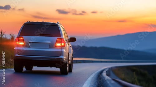 A silver SUV drives along a winding mountain road at dusk, its glowing taillights shining against a stunning sunset, evoking a feeling of freedom and adventure