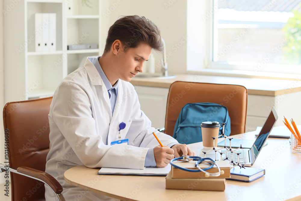 Male medical intern writing at table in clinic Male medical intern writing at table in clinic