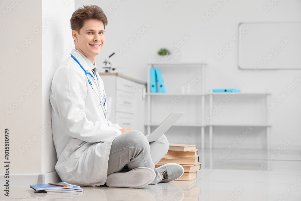 Male medical intern using laptop on floor in clinic Male medical intern using laptop on floor in clinic
