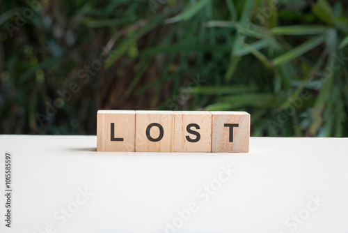Lost, word written on square wood block, on top of white table with palm plant at the background.