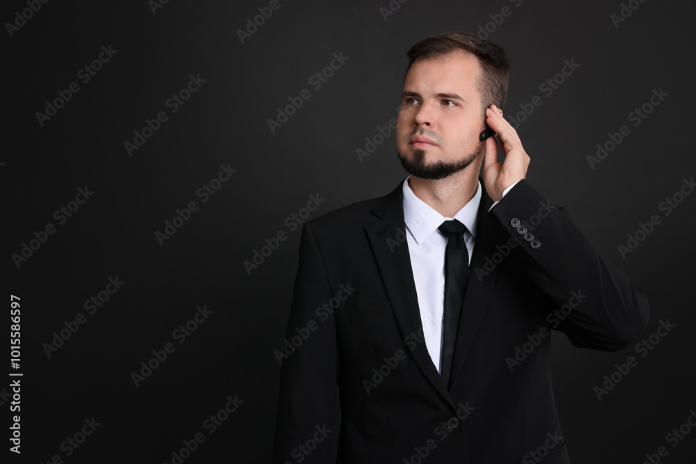 Young bodyguard in suit with earpiece on black background, space for text Young bodyguard in suit with earpiece on black background, space for text