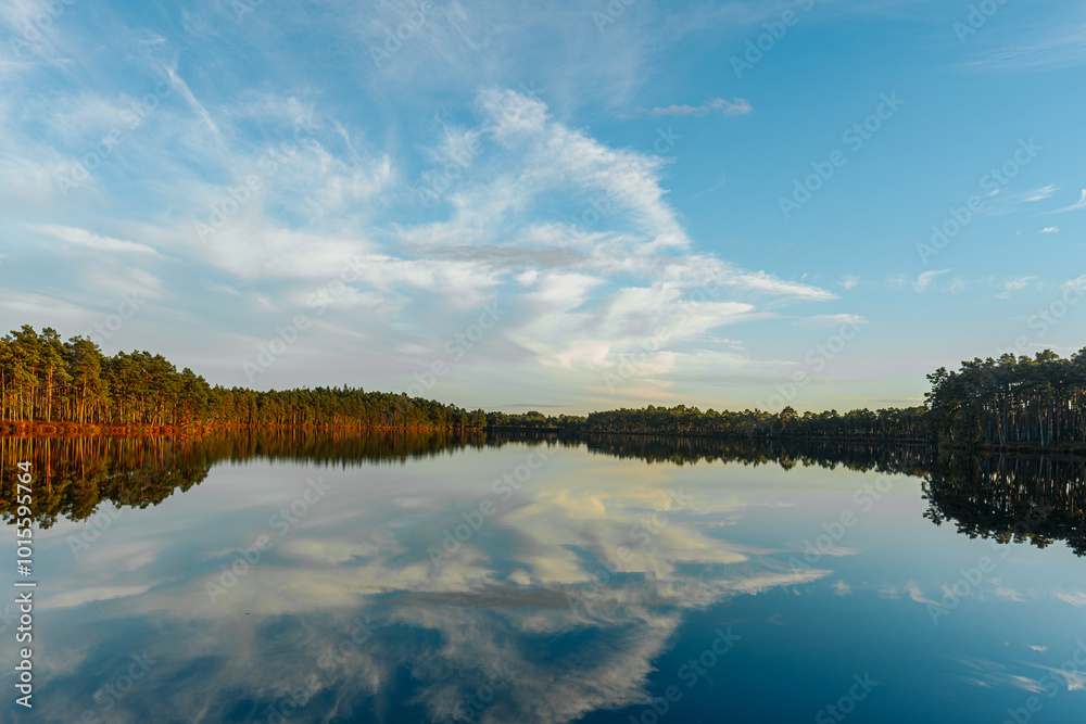 A serene landscape featuring a crystal-clear lake reflecting the blue sky, white clouds, and tree-lined shore. The still water and vibrant sky create a peaceful and harmonious scene. A serene landscape featuring a crystal-clear lake reflecting the blue sky, white clouds, and tree-lined shore. The still water and vibrant sky create a peaceful and harmonious scene.