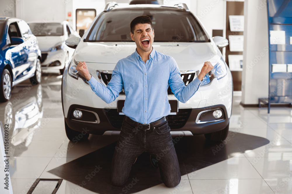 New Auto. Excited Man Shouting Shaking Fists Celebrating Buying New Car Standing On Knees In Dealership Store New Auto. Excited Man Shouting Shaking Fists Celebrating Buying New Car Standing On Knees In Dealership Store