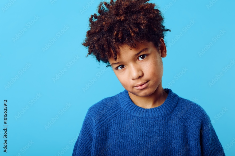 joyful young african american boy with afro hair wearing a blue sweater against a matching blue background joyful young african american boy with afro hair wearing a blue sweater against a matching blue background