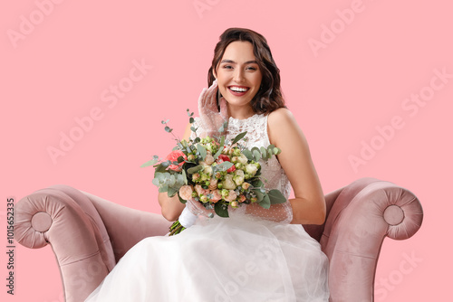 Beautiful bride with wedding bouquet in armchair on pink background photo