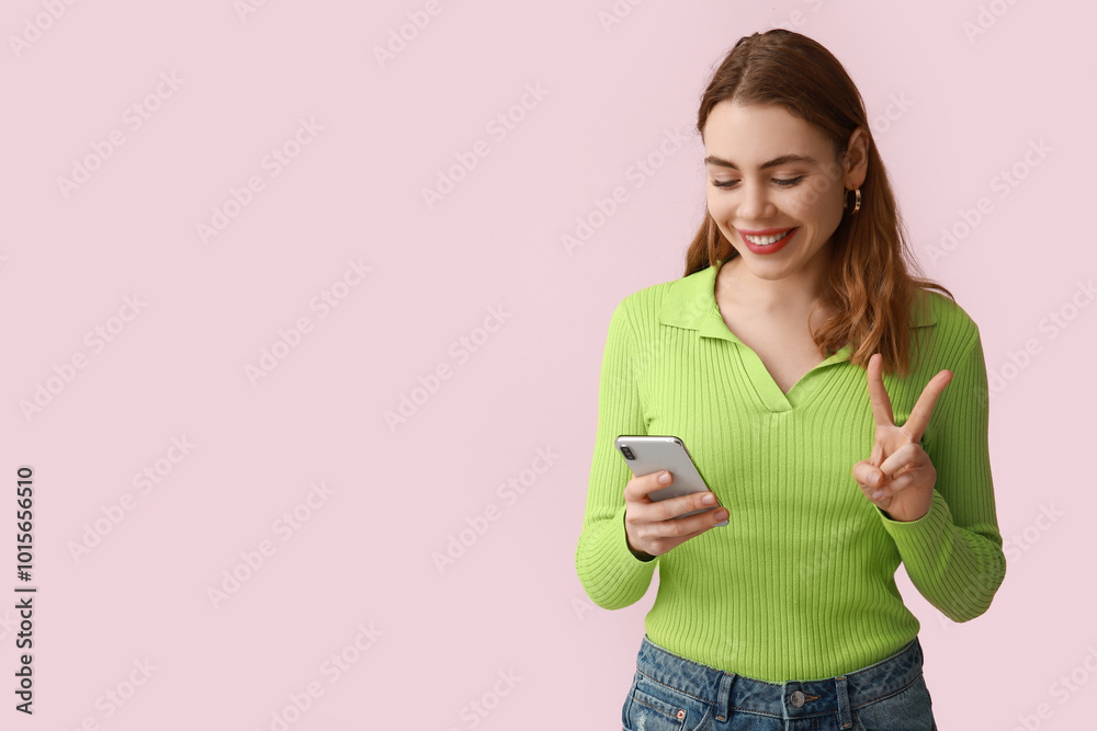 Pretty young woman showing peace gesture while video chatting on pink background