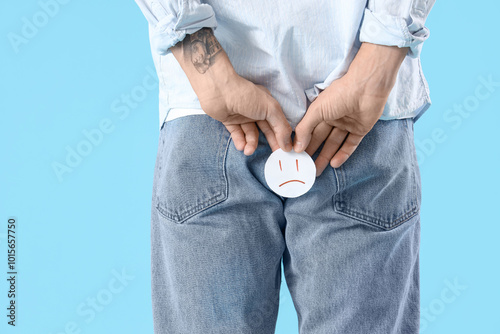 Young man with hemorrhoids and sad smile on blue background, back view
