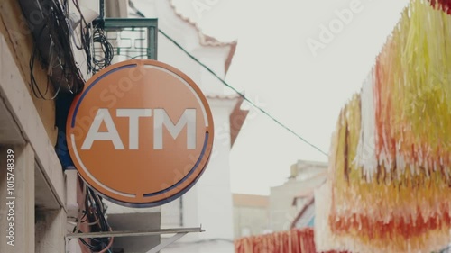 Orange ATM sign in a Portuguese street with colorful festive decorations and traditional architecture. Outdoor Orange ATM Sign in Portuguese Street
