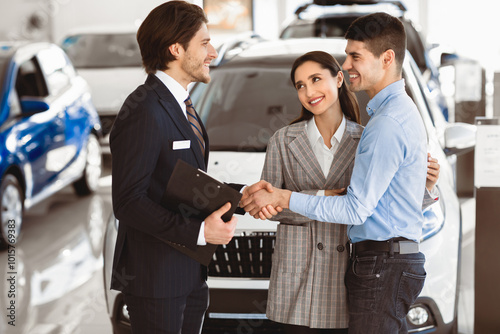 Pleasure Working With You. Beautiful couple embracing after buying new car, shaking hands with salesman