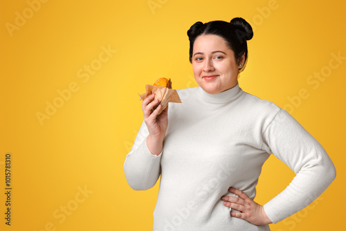 Fotografía Beautiful plump woman posing with burger in hand over yellow background and smil