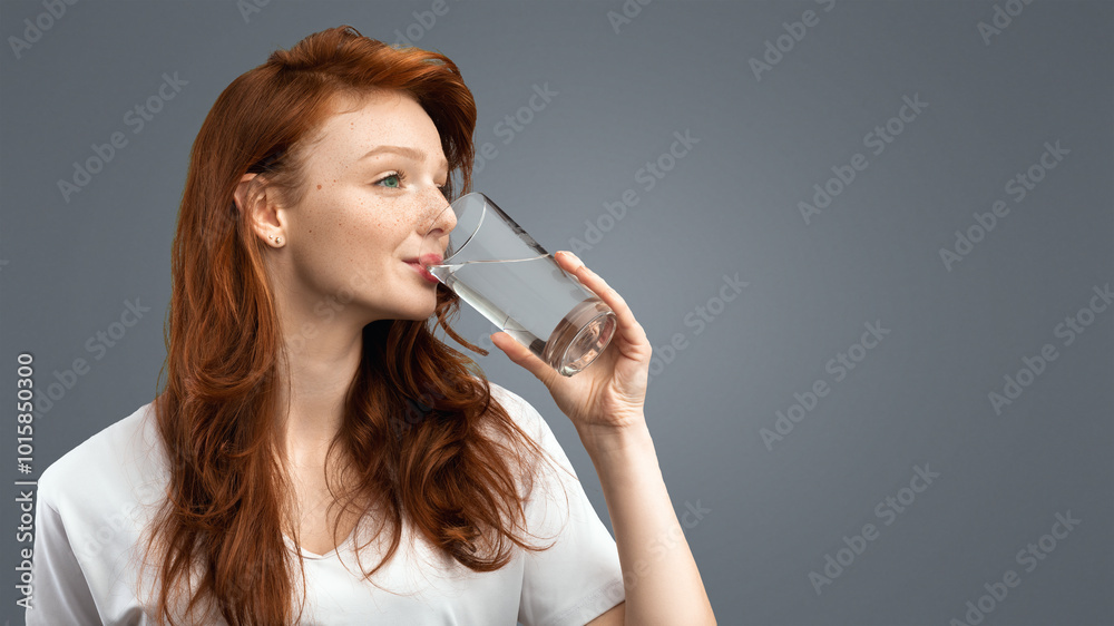 Healthy Hydration. Red-Haired Millennial Woman Drinking Water From Glass Standing Over Gray Studio Background, Wearing Casual T-Shirt. Side View Shot. Stay Hydrated Concept Healthy Hydration. Red-Haired Millennial Woman Drinking Water From Glass Standing Over Gray Studio Background, Wearing Casual T-Shirt. Side View Shot. Stay Hydrated Concept
