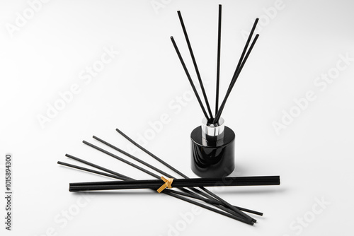 A minimalist display of essential oil and black diffuser sticks on a clean white background