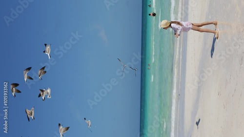 A child on the beach feeds the birds.A sunny day on the seashore, seagulls flutter in the air.The girl throws pieces of food, and the seagulls catch them on the fly.The ocean is a beautiful blue color