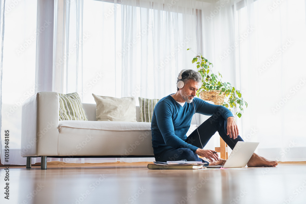 Homeoffice for handsome man. Man sitting on floor and working on laptop with headphones on head. Telecommuting. Homeoffice for handsome man. Man sitting on floor and working on laptop with headphones on head. Telecommuting.