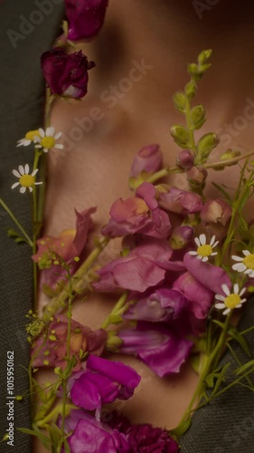 Vertical closeup of beautiful bouquet of purple wildflowers in focused foreground and fragile chest of anonymous woman in blurred background photo