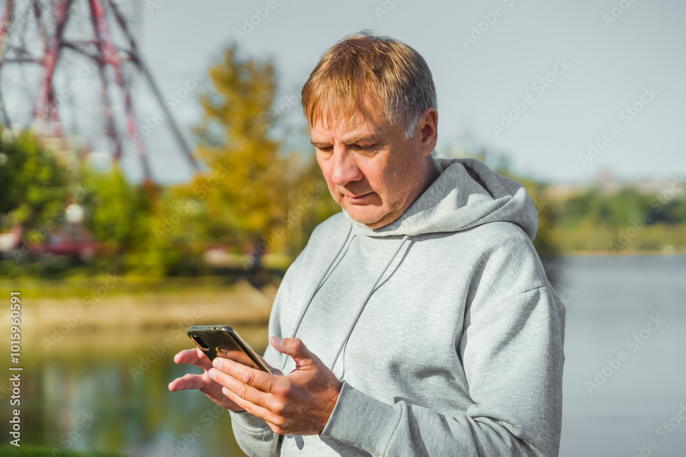 Man in hoodie with mobile phone resting after training in park Man in hoodie with mobile phone resting after training in park