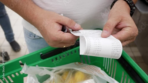 Buyer checking a receipt for paying for groceries in a store near the cash register against the backdrop of a grocery cart. Shopping at the supermarket. Product prices.