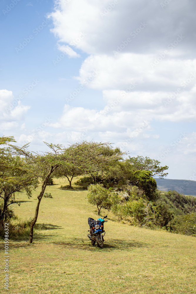 A motorbike parked under a tree next to a cliff in the countryside A motorbike parked under a tree next to a cliff in the countryside