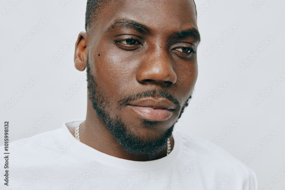 Portrait of a thoughtful young man with a serious expression, wearing a plain white t shirt and a subtle chain necklace, set against a light grey background Portrait of a thoughtful young man with a serious expression, wearing a plain white t shirt and a subtle chain necklace, set against a light grey background
