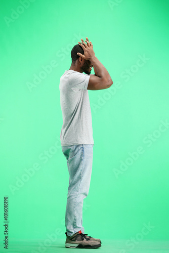 A man, full-length, on a green background, clutched his head