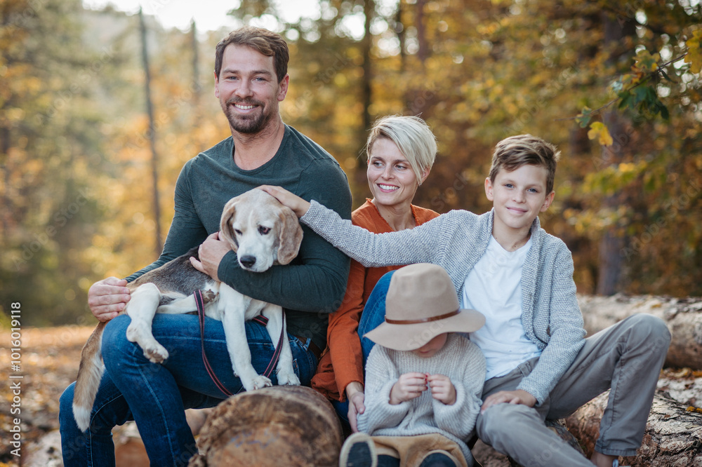 Fototapeta premium Portrait of family sitting in the middle autumn forest. Nuclear family with dog spending weekend outdoors.