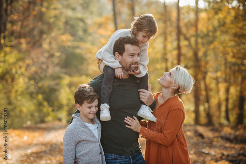 Young family with small children on walk in autumn forest. Father carrying daughter on his shoulders.