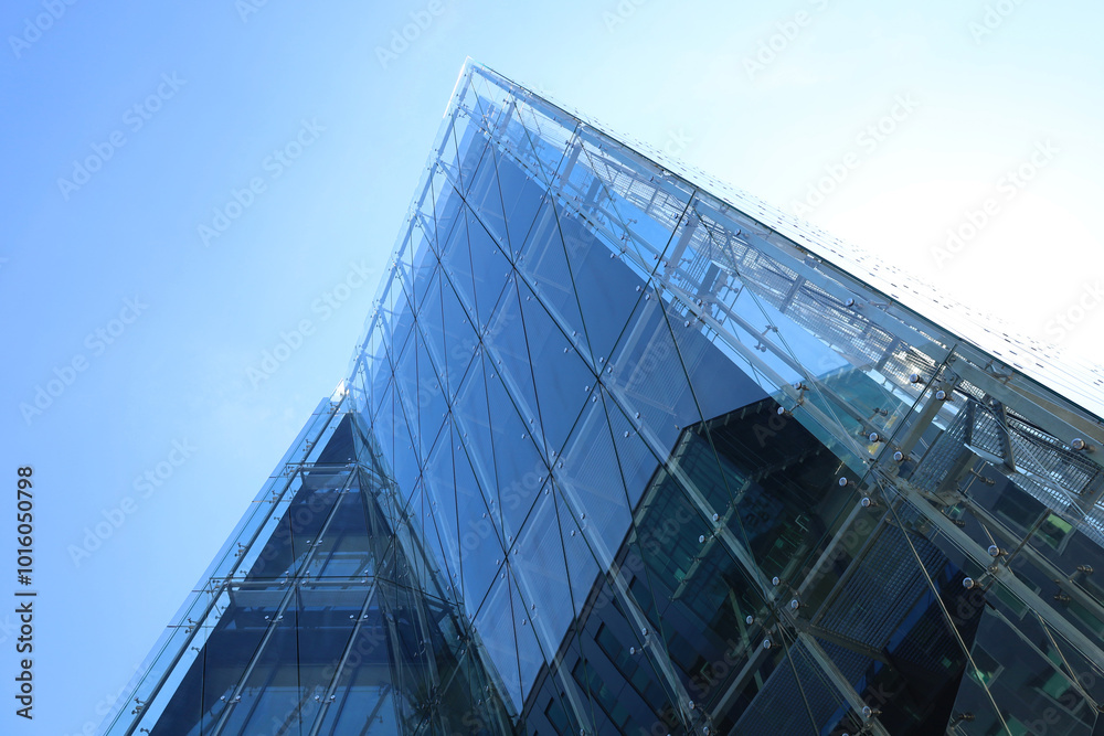 Perspective view from below to corner of office building made of toned glass and steel constructions under blue sky. Fragment of skyscraper facade. Modern house background.