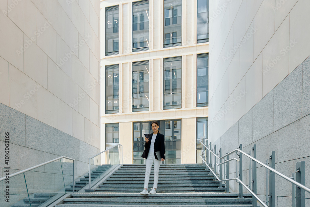 Fototapeta premium Young European woman with laptop in hands stands at the entrance to the company's central office